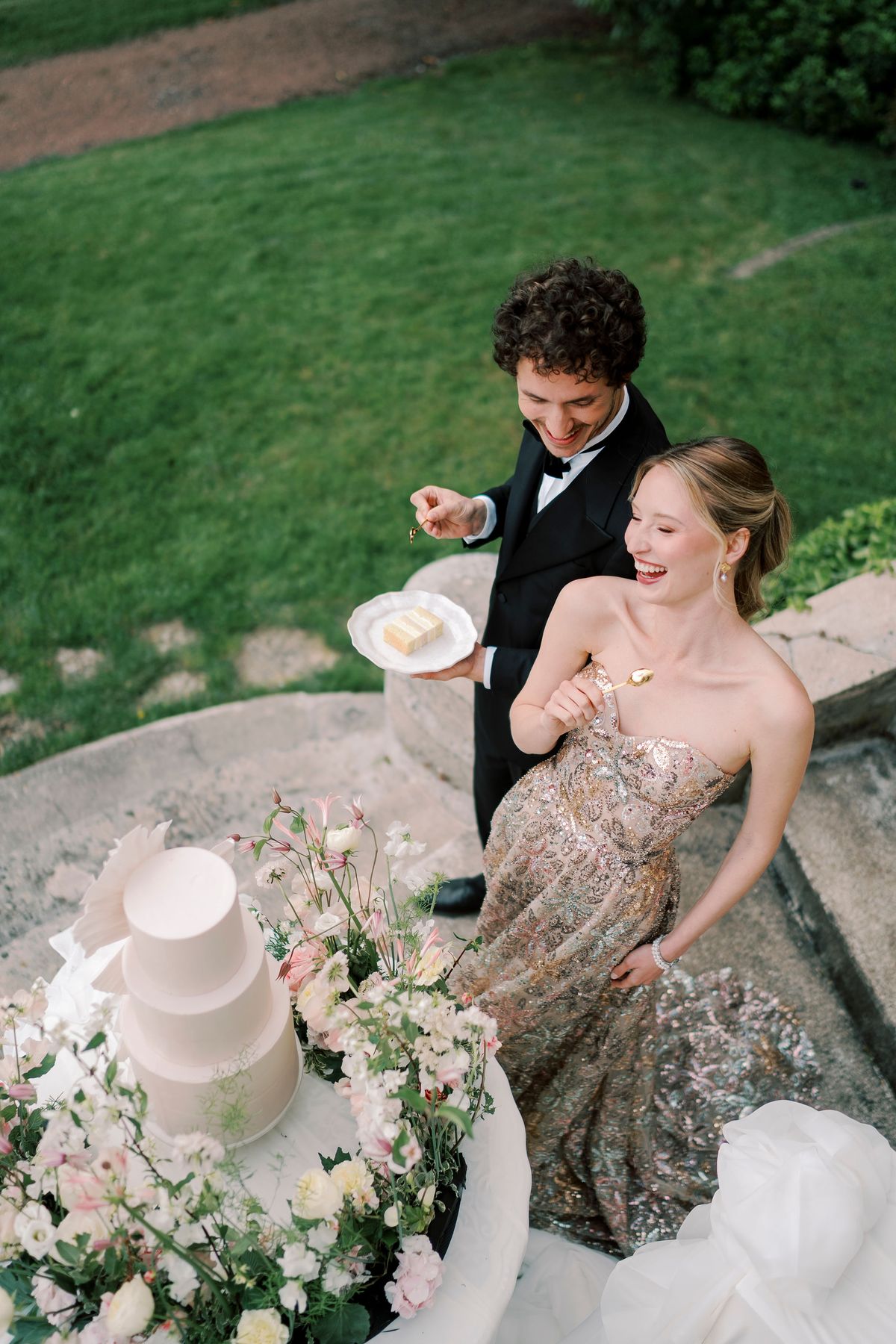 Lucien holding a slice of cake as Amélie laughs beside the tiered cake