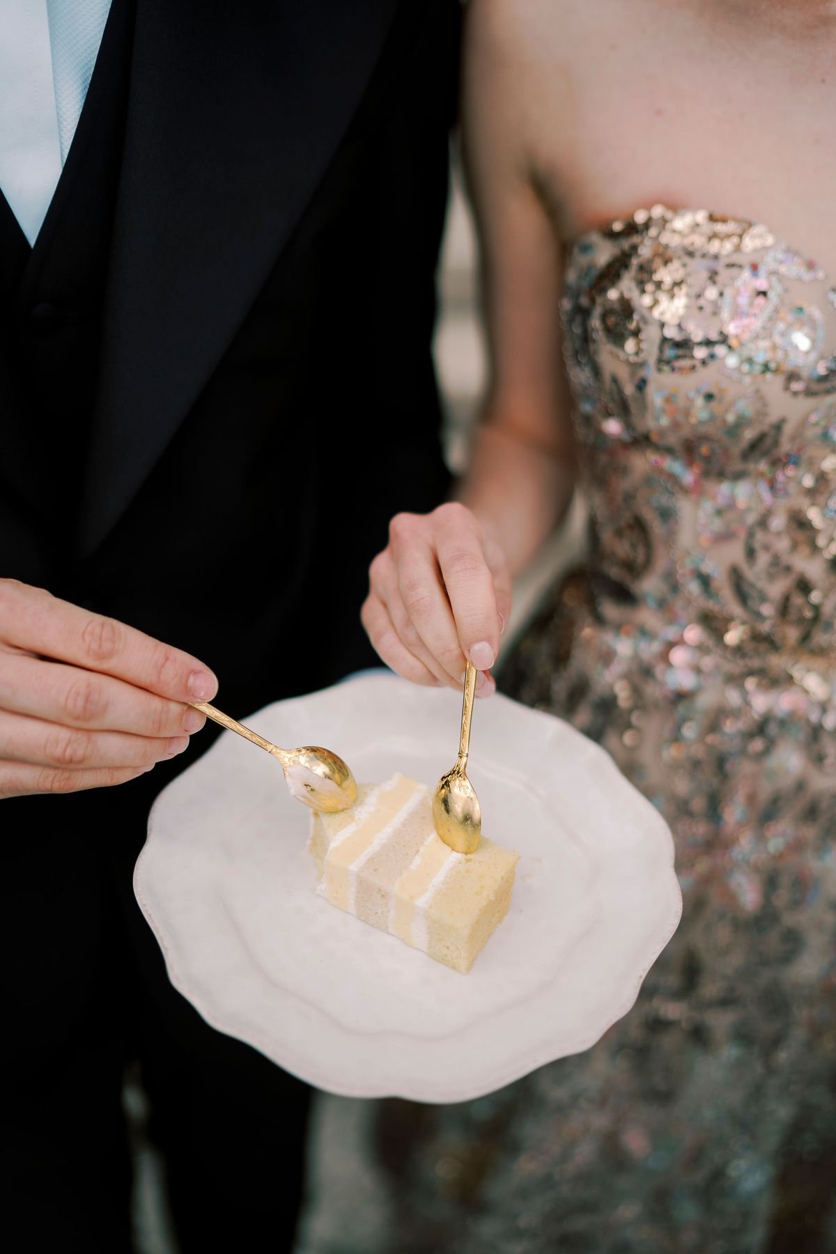 Close-up of two gold forks and a slice of cake on a scalloped white plate