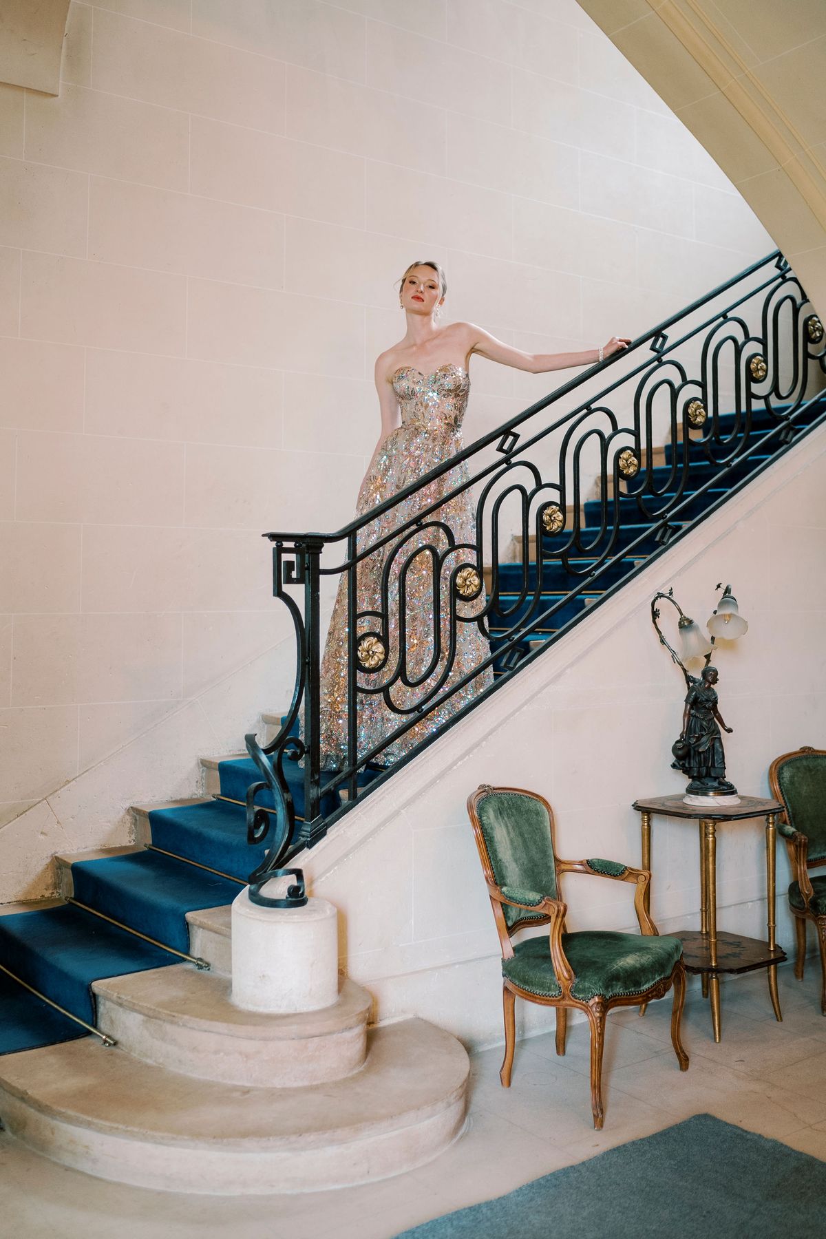 Amélie in a sequined gown on a curved staircase with a wrought-iron banister, Château du Prieuré
