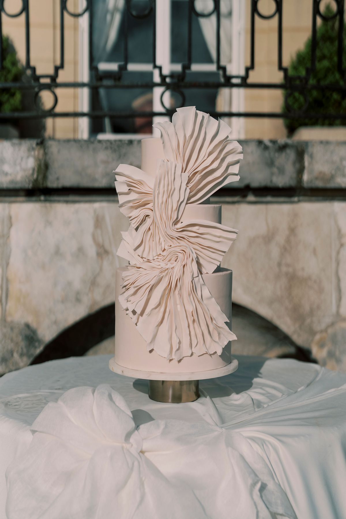 Tiered white cake with a tier wrapped in pleated folds, on the terrace at Château du Prieuré