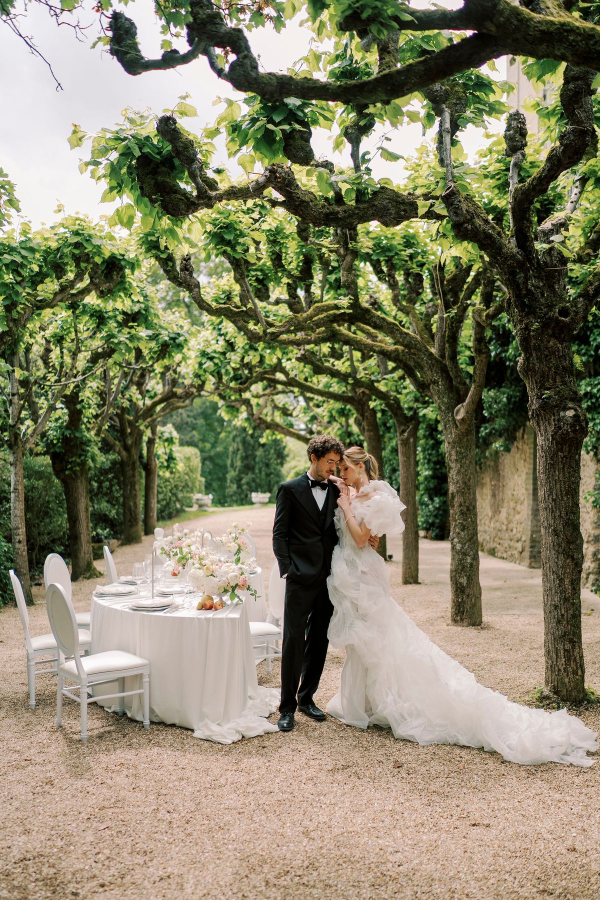 Amélie and Lucien embracing beside the serpentine table beneath the pleached trees