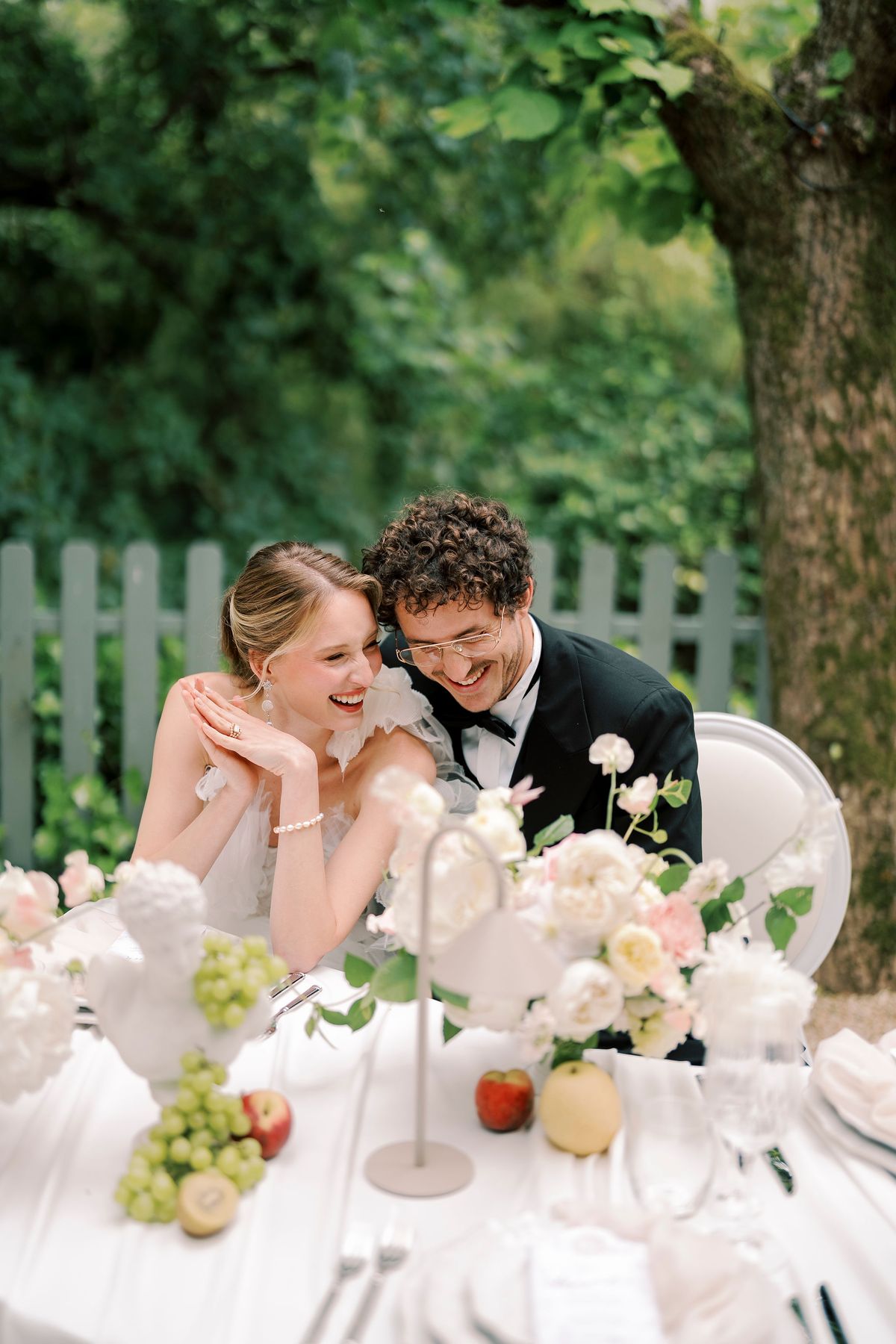 Amélie and Lucien laughing at the dinner table behind fruit and flowers
