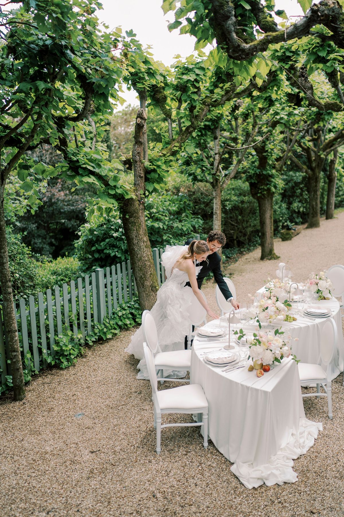 Amélie and Lucien arranging place settings at the serpentine table in the tree-lined alley