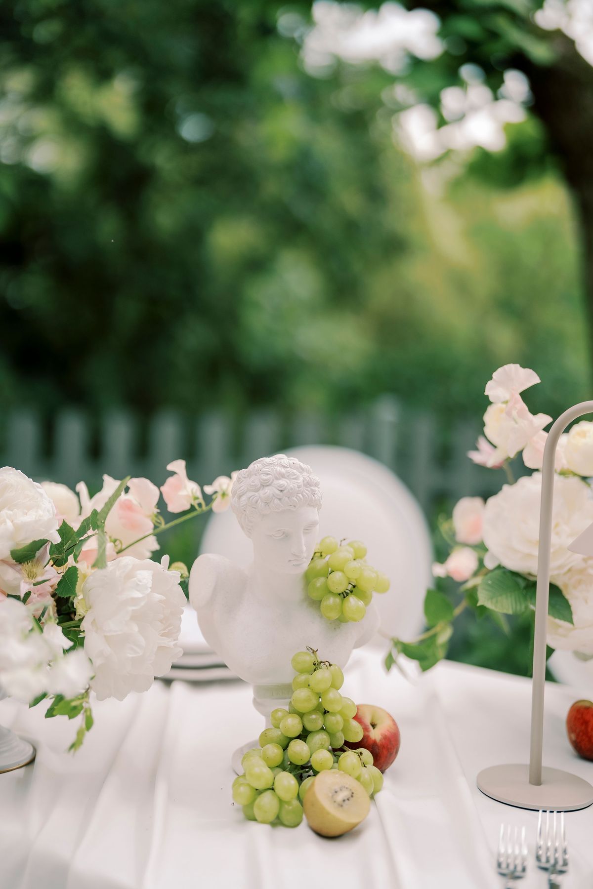 Green grapes, an apple and a kiwi around a white plaster bust on the dinner table