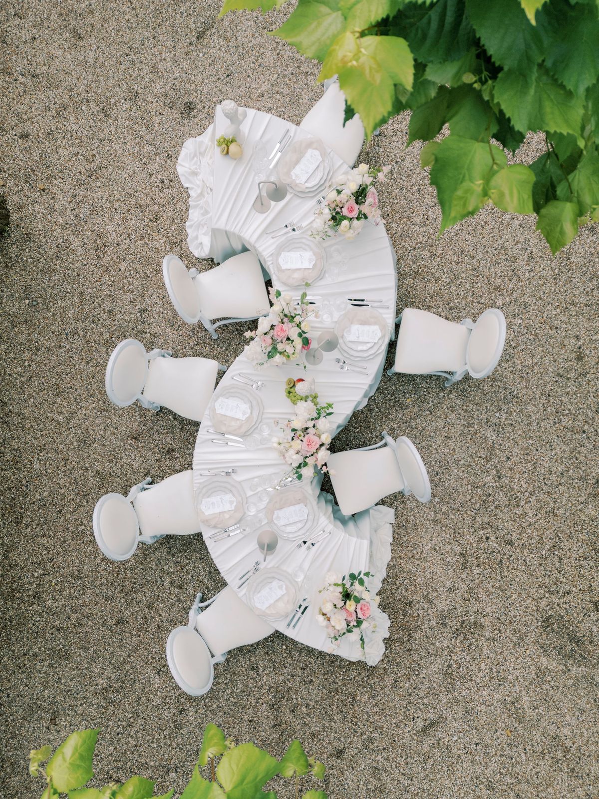 Overhead view of the serpentine dinner table on gravel, white chairs and flowers along its curve