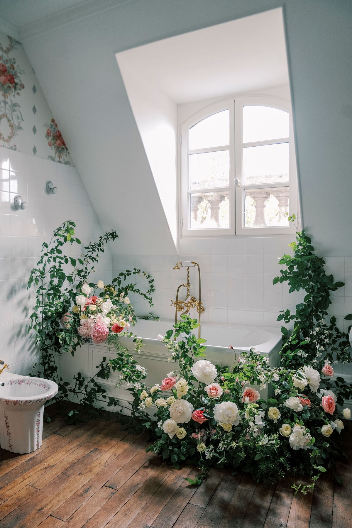Bathtub under a sloping attic window surrounded by climbing greenery and garden roses, Château du Prieuré