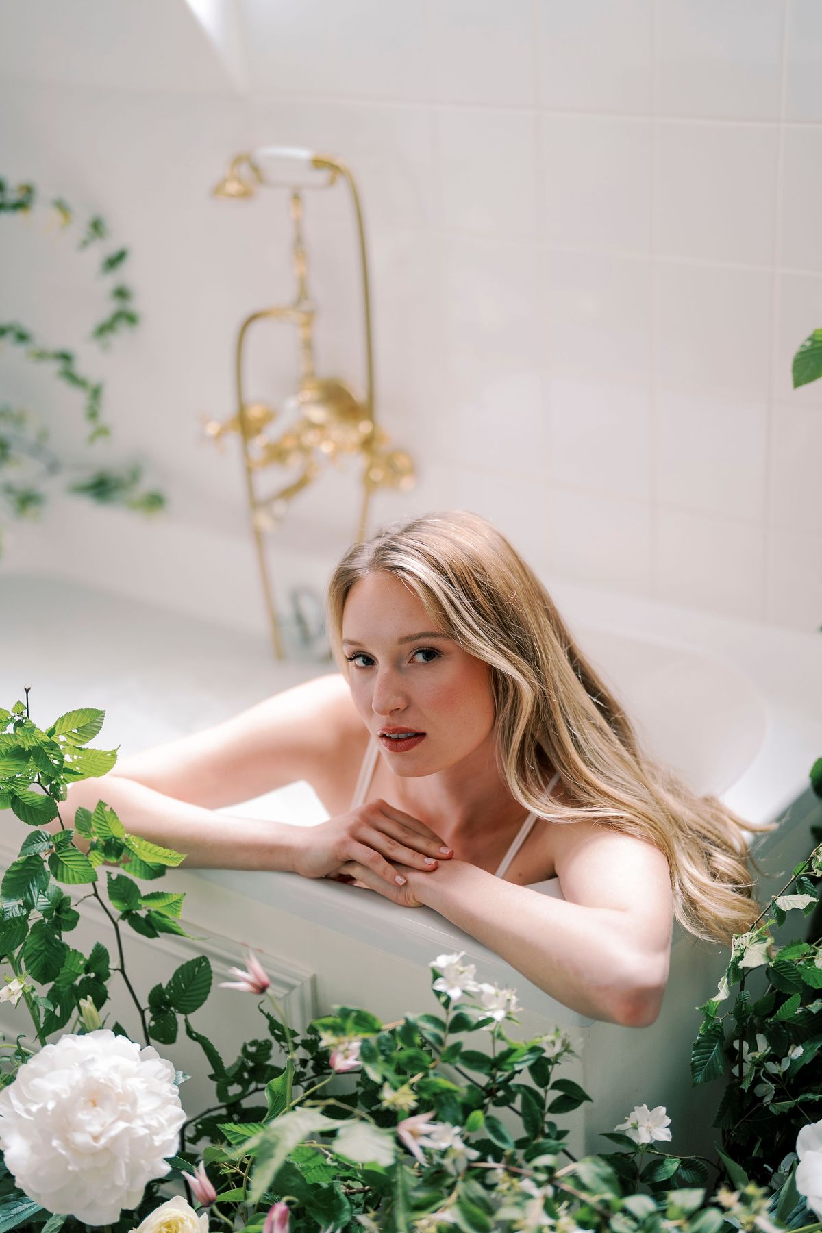 Amélie resting her arms on the edge of the bathtub, white roses and greenery around her