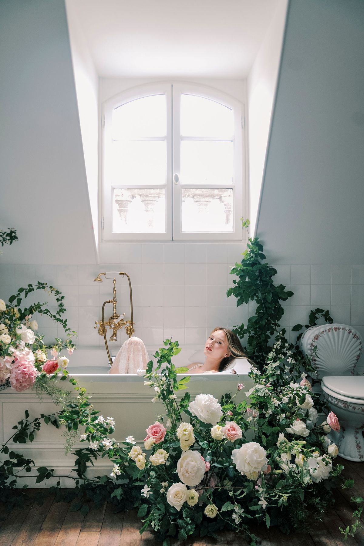 Amélie lying back in the bathtub among garden roses and greenery in the attic bathroom