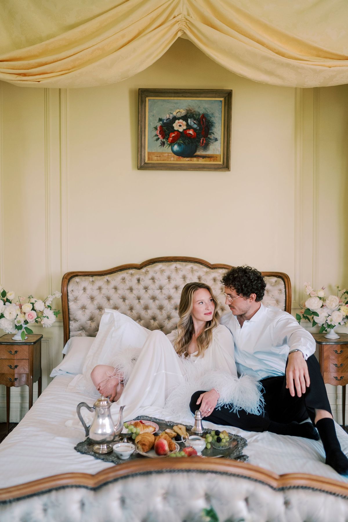 Amélie and Lucien on the bed with a silver breakfast tray of croissants and fruit