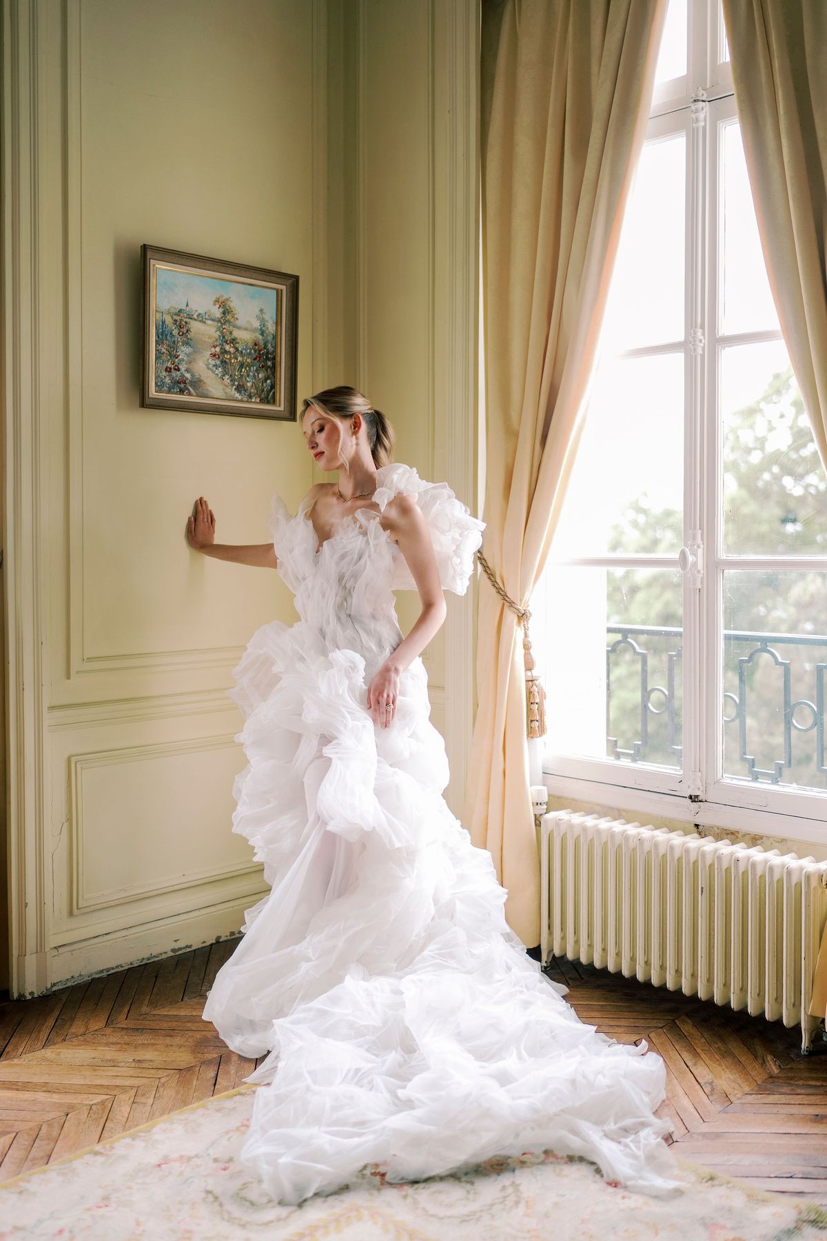 Amélie in her ruffled organza gown, one hand on the panelled wall of the yellow bedroom