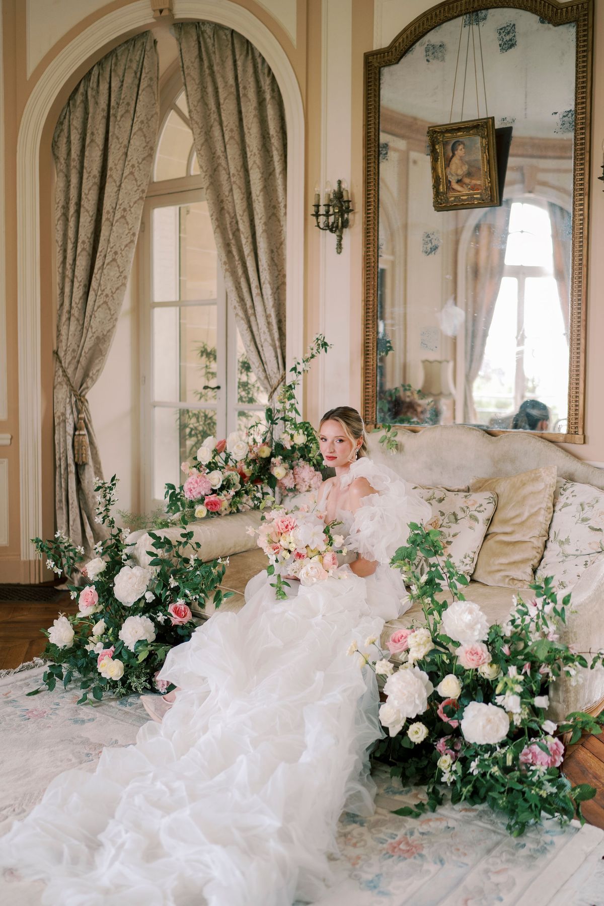 Amélie on a salon sofa with her bouquet, the organza skirt pooled over the rug