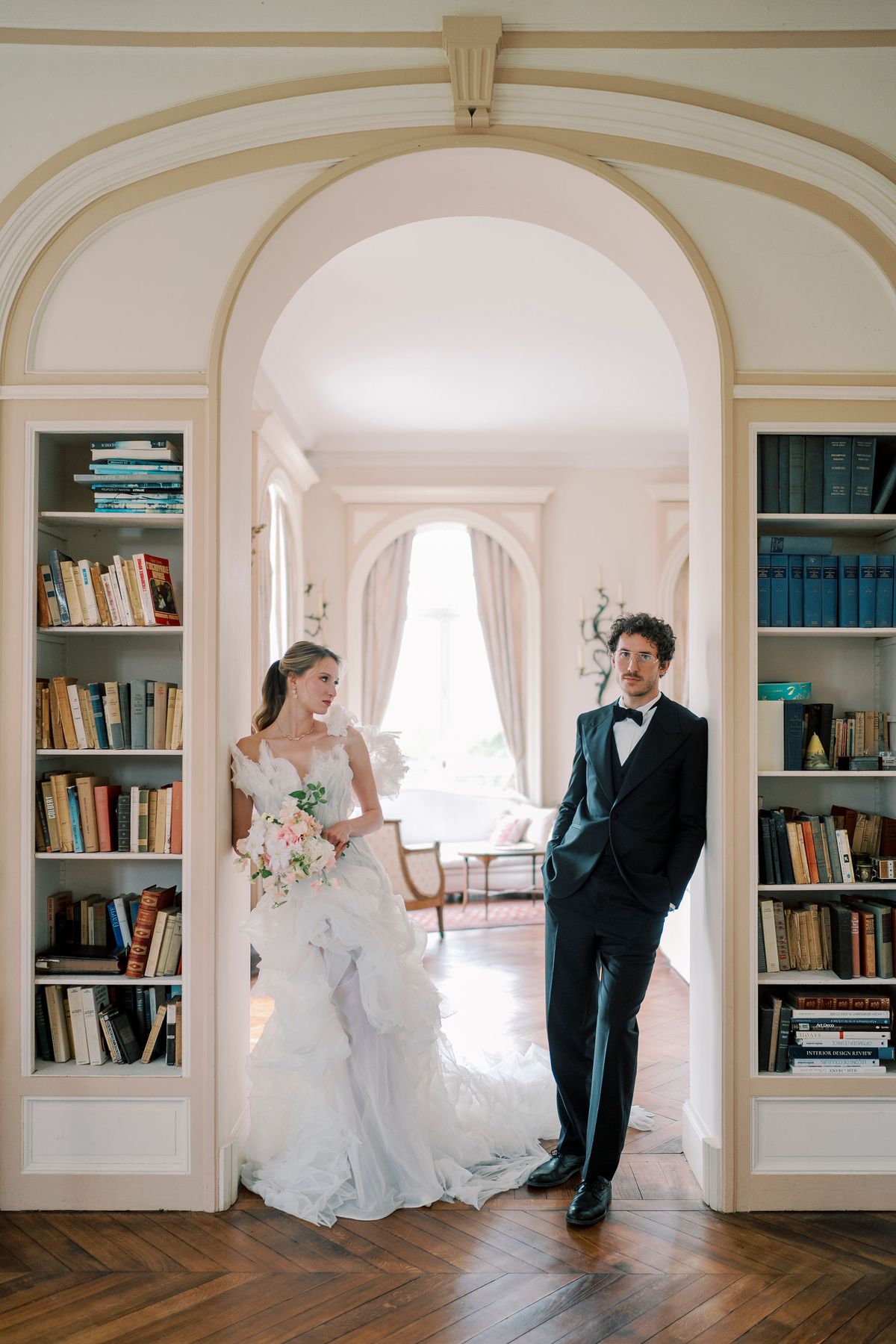 Amélie and Lucien standing either side of an arched doorway lined with bookshelves