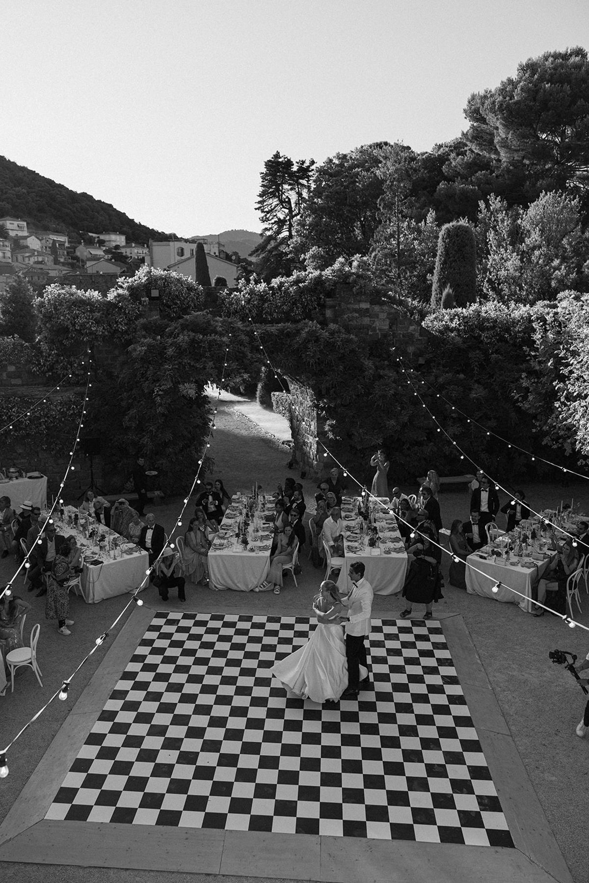 In black and white, a high view of a chequered dance floor with a couple dancing and dinner tables around it.