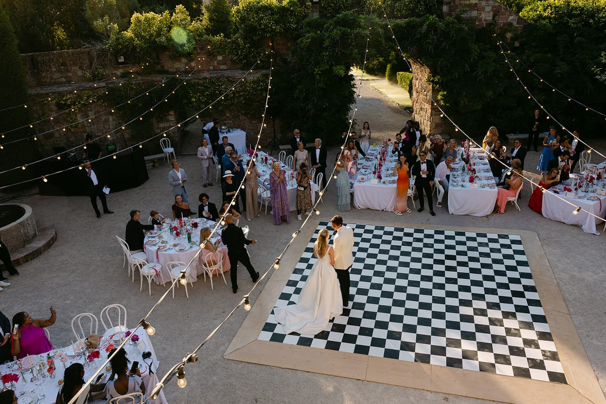 Seen from above, the couple stand on a checkerboard dance floor in a courtyard surrounded by guests and dinner tables.