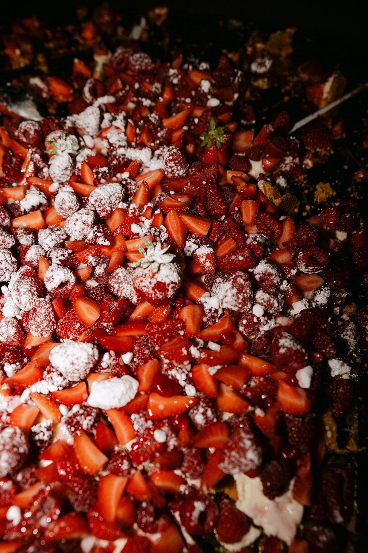 A close-up of a dessert covered in sliced red strawberries and white meringue pieces.