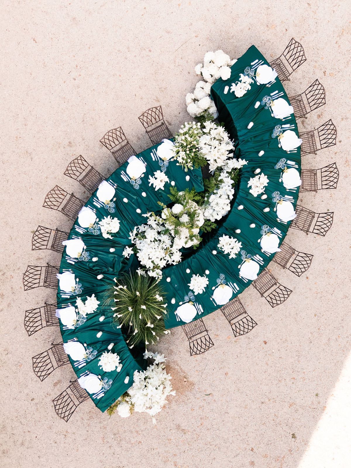 Overhead view of a long banquet table dressed in deep green linen and white flowers on the gravel terrace at Château de Sannes, Provence