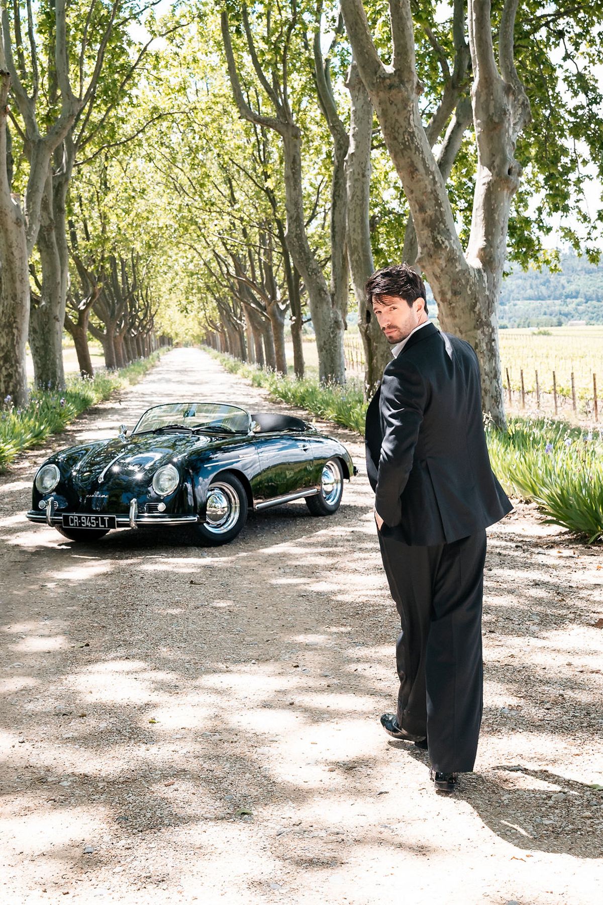Groom walking toward a vintage open-top Porsche parked on the plane-tree avenue at Château de Sannes, Provence