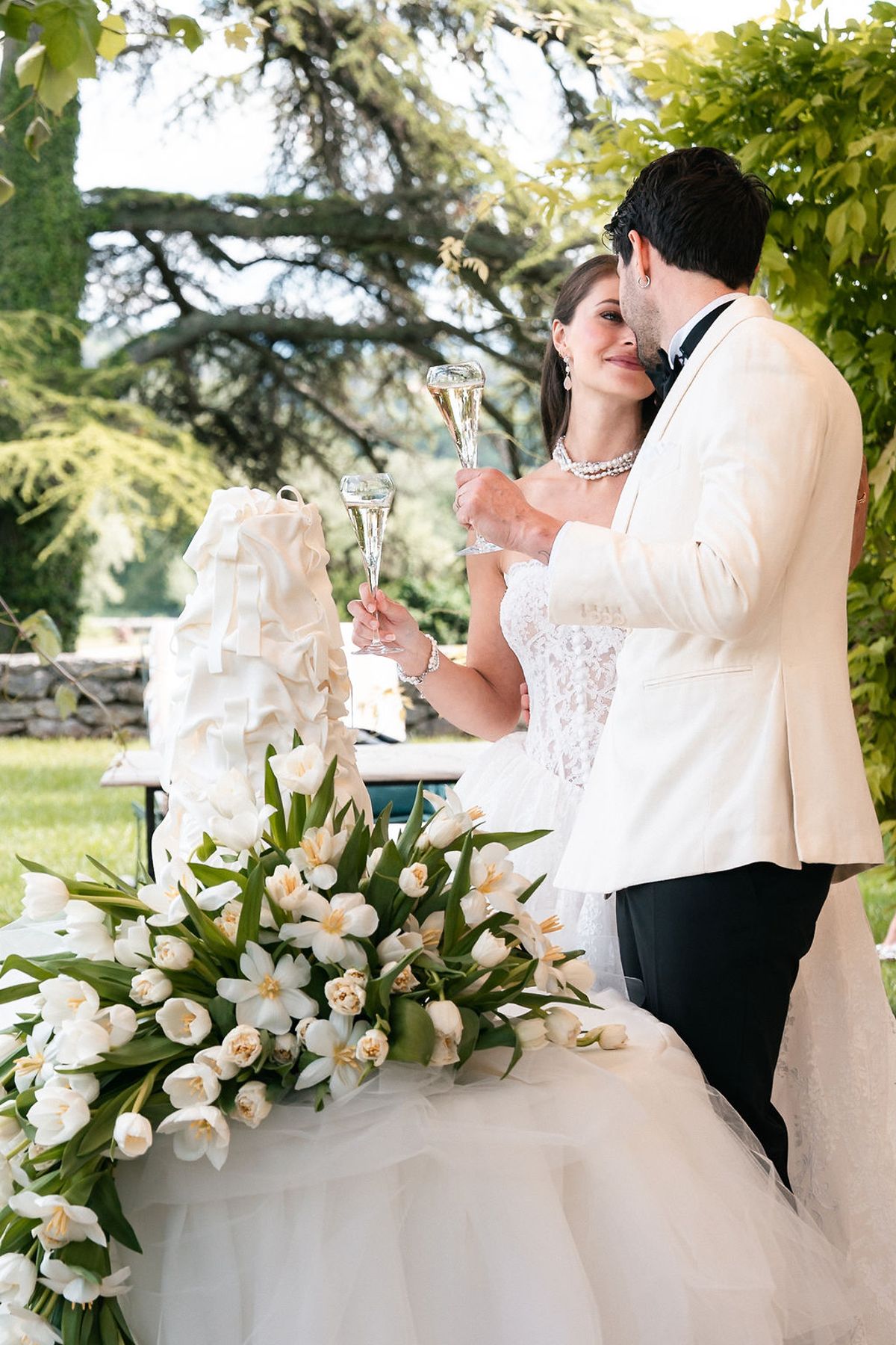 Bride and groom at the cake table banked with white tulips and roses at Château de Sannes, Provence