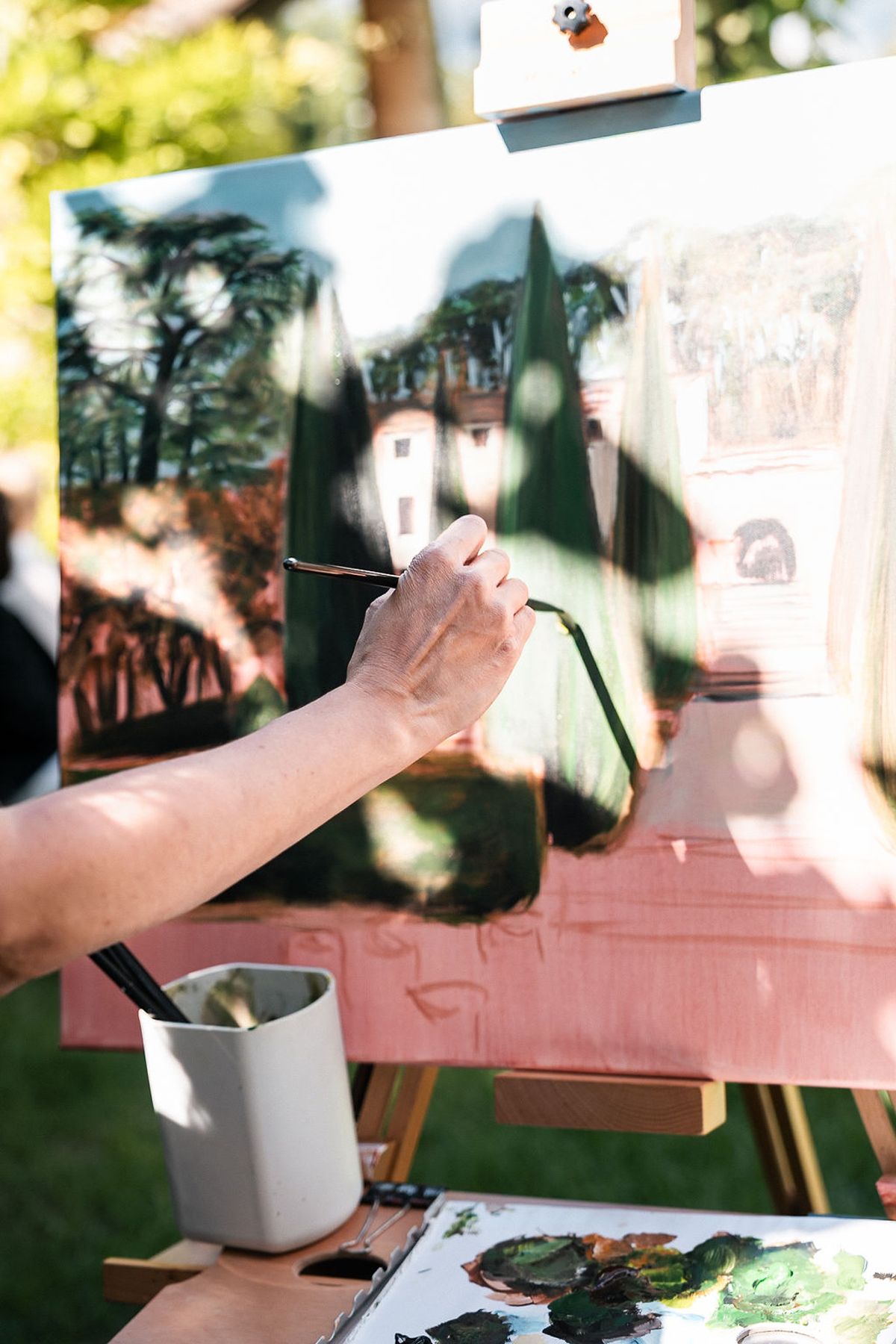A painter working in oils at an easel, the canvas showing the cypress garden at Château de Sannes, Provence
