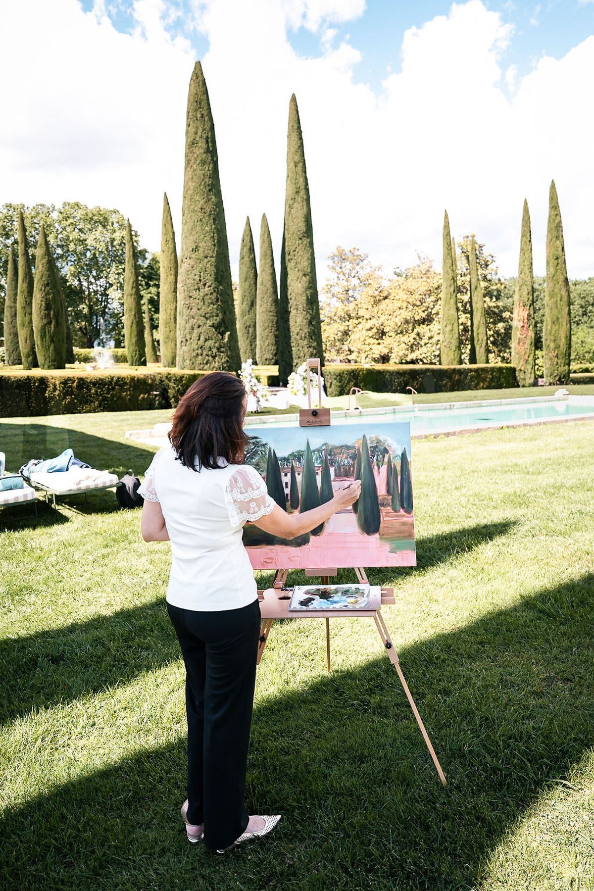 A painter at an easel on the lawn working on a canvas of the ceremony setting at Château de Sannes, Provence