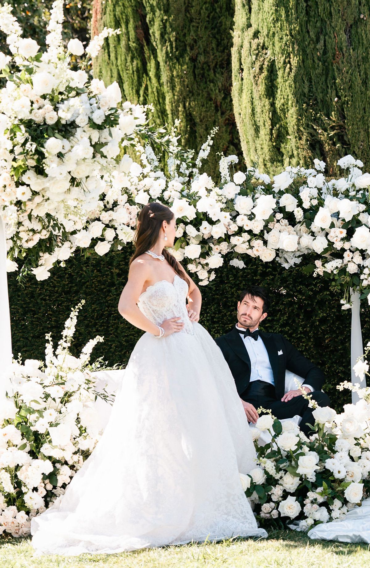 Bride standing and groom seated at the white floral ceremony installation at Château de Sannes, Provence