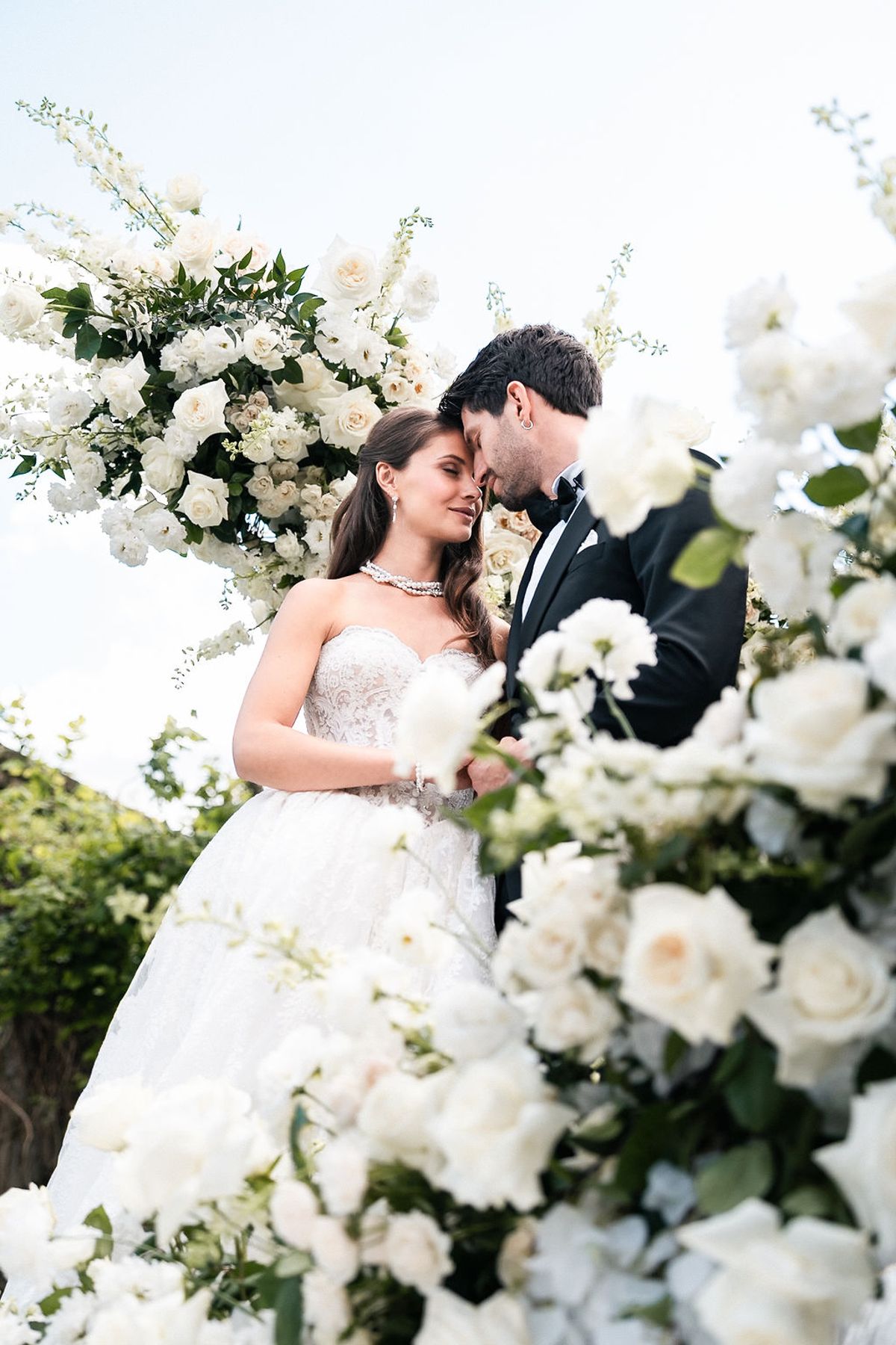 Bride and groom photographed through a white floral installation of roses and lilies at Château de Sannes, Provence