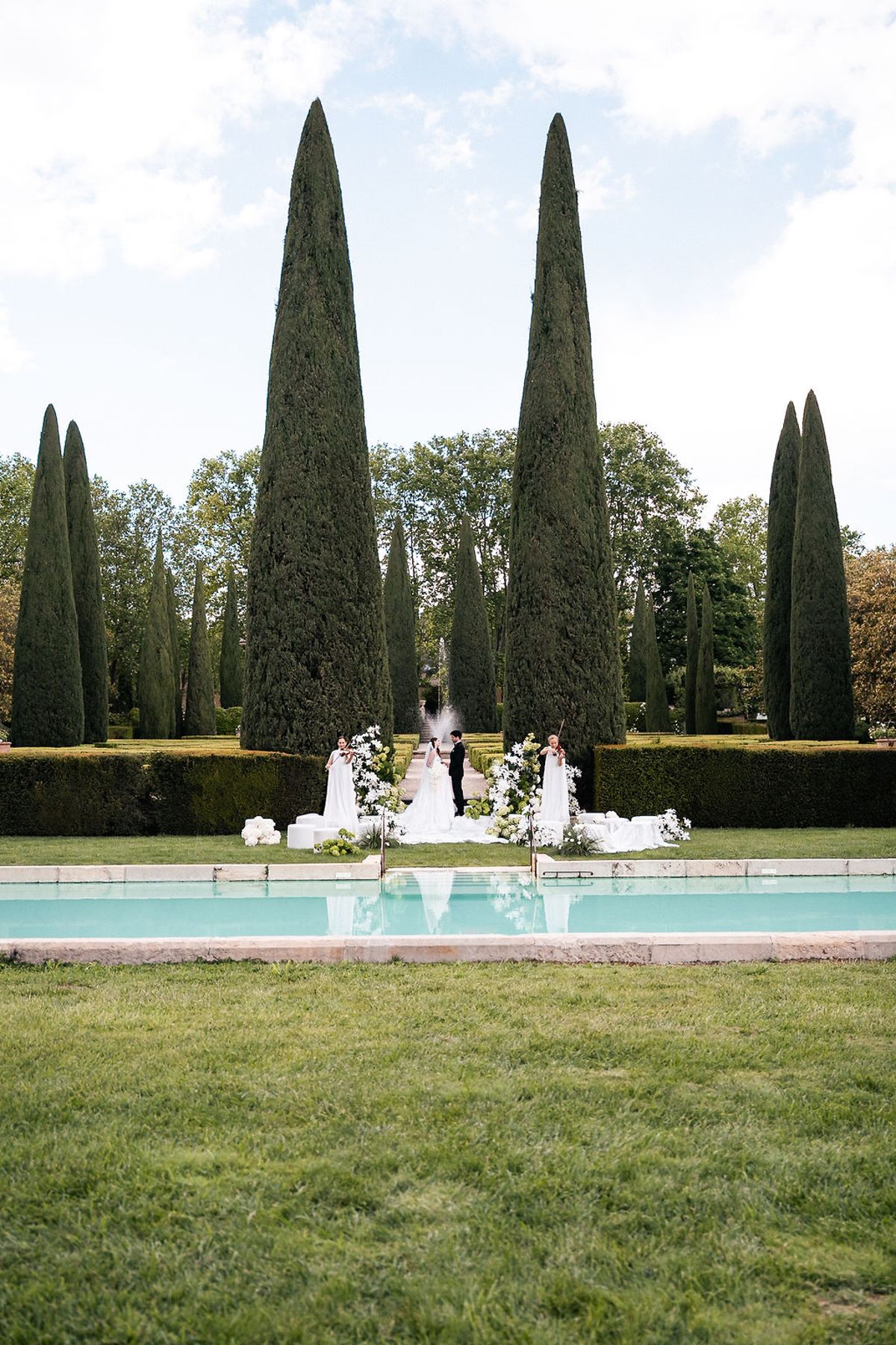 The formal garden seen across the swimming pool, with tall cypresses lining the lawn at Château de Sannes, Provence