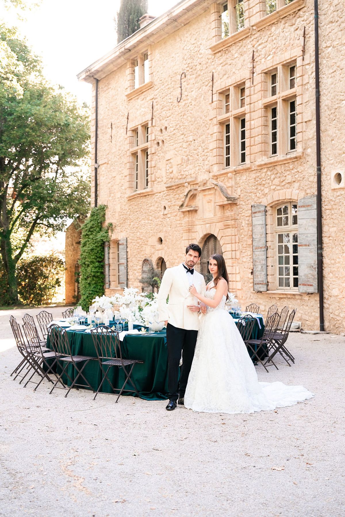 Bride and groom beside a round table in deep green linen before the stone façade at Château de Sannes, Provence