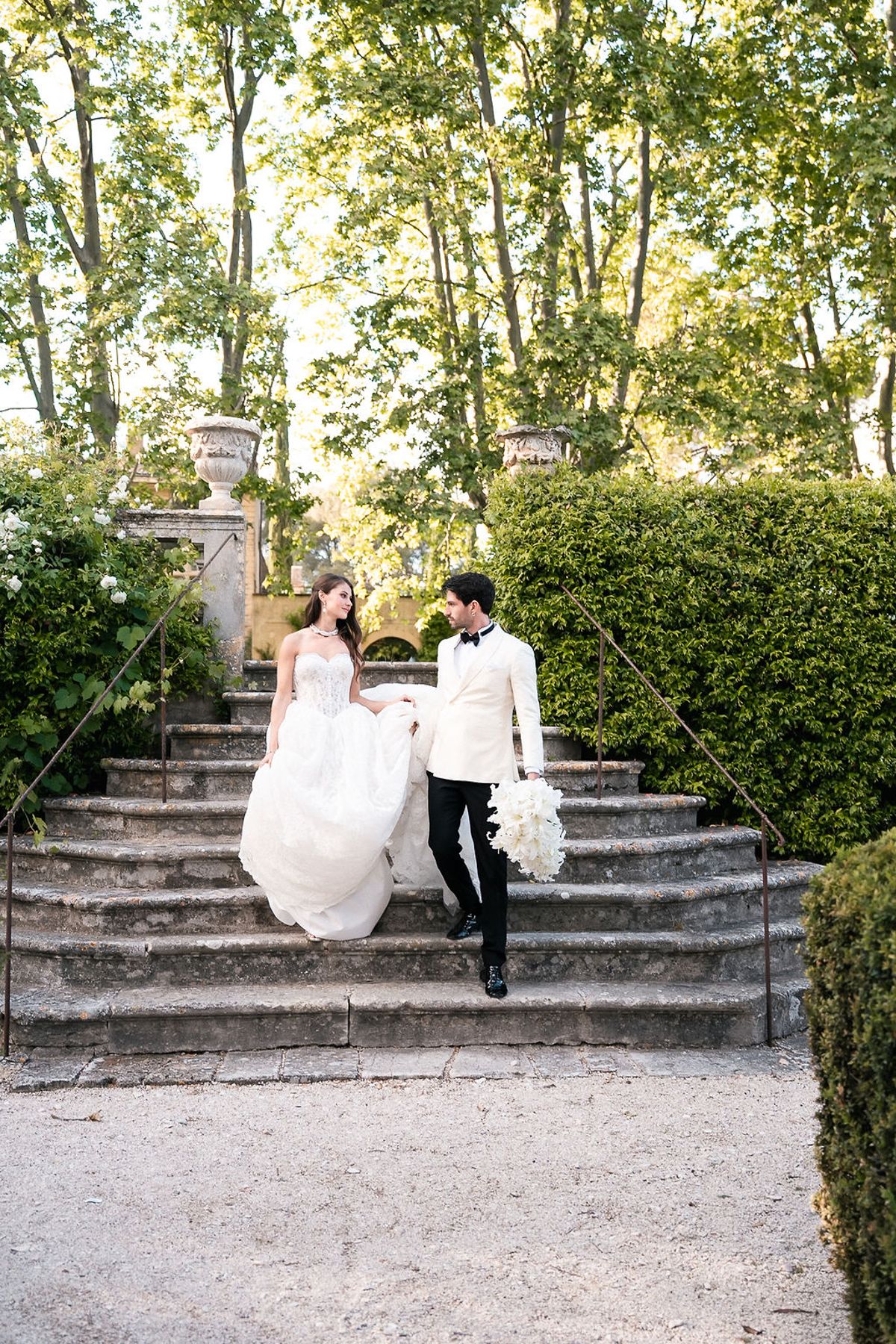 Bride and groom walking down the stone garden steps between clipped hedges at Château de Sannes, Provence