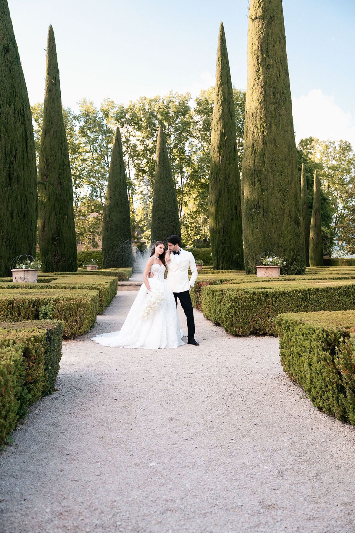 Bride and groom on the gravel walk between box parterres and cypresses at Château de Sannes, Provence
