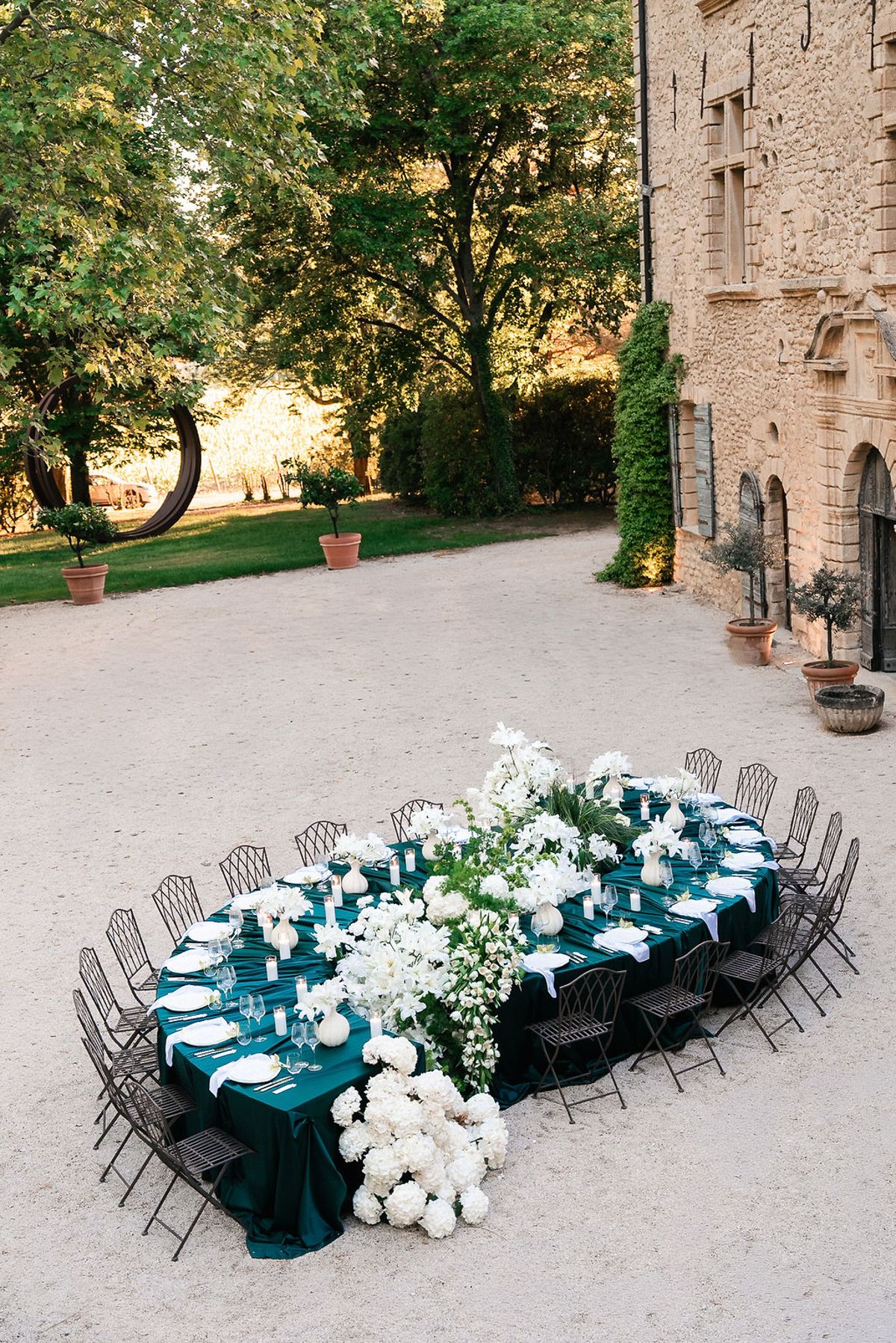 Banquet table in deep green linen banked with white hydrangeas on the gravel beside the château at Château de Sannes, Provence