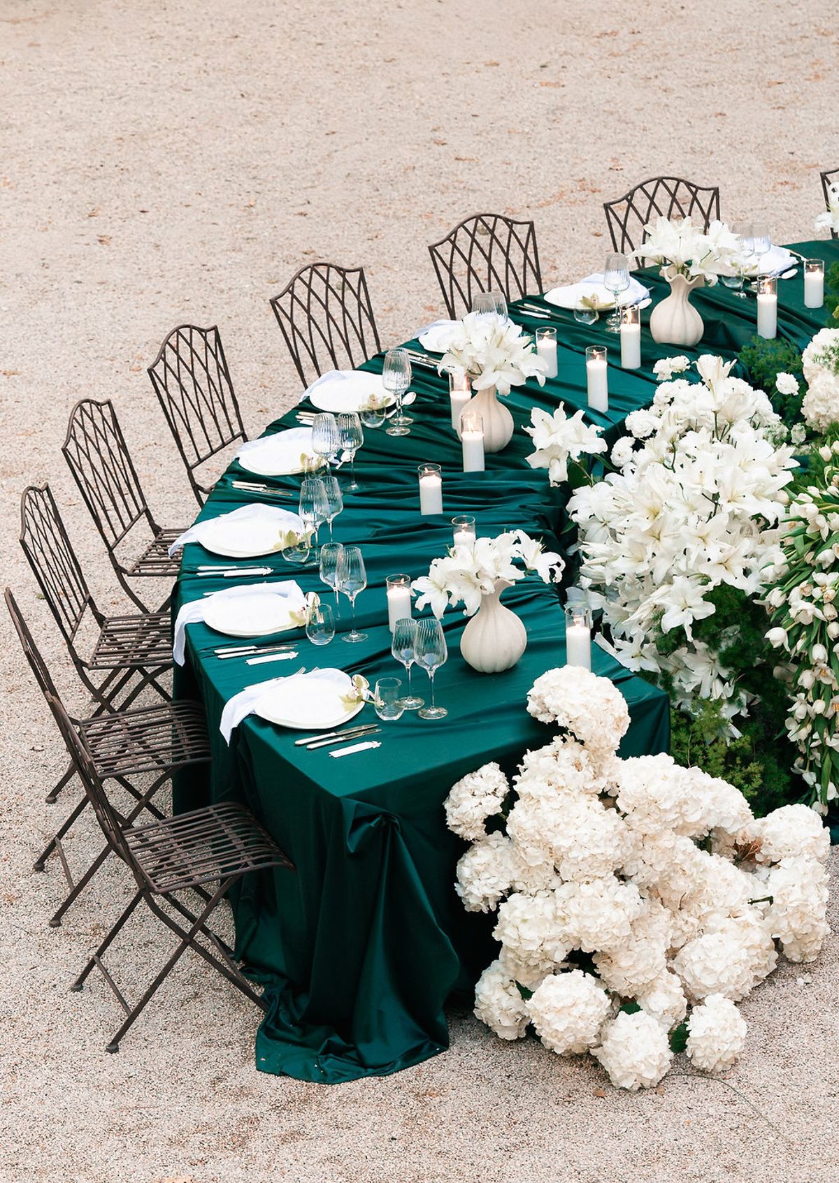 Long banquet table in deep green linen set with white hydrangeas, candles and metal bistro chairs at Château de Sannes, Provence