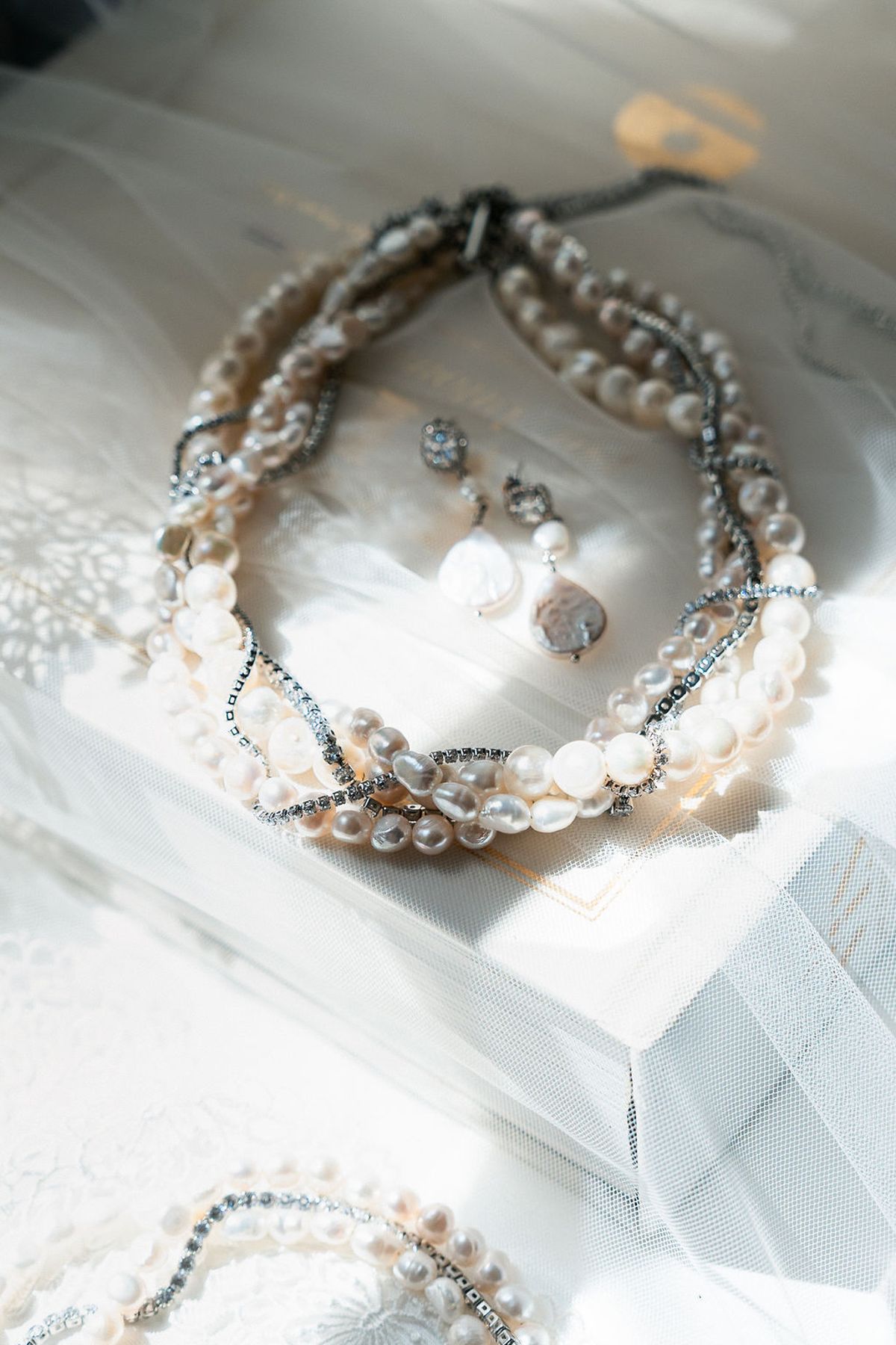 Layered pearl necklaces and drop earrings photographed on white silk at Château de Sannes, Provence