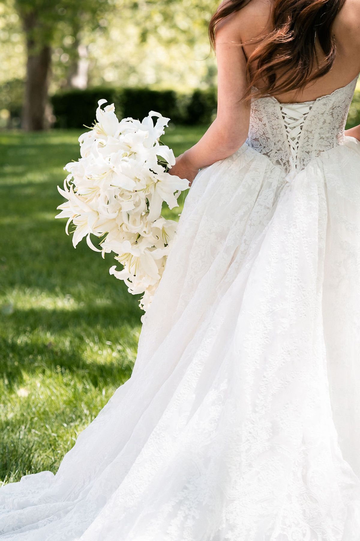 Bride seen from behind, showing the corset lacing of the gown and a cascading white bouquet at Château de Sannes, Provence