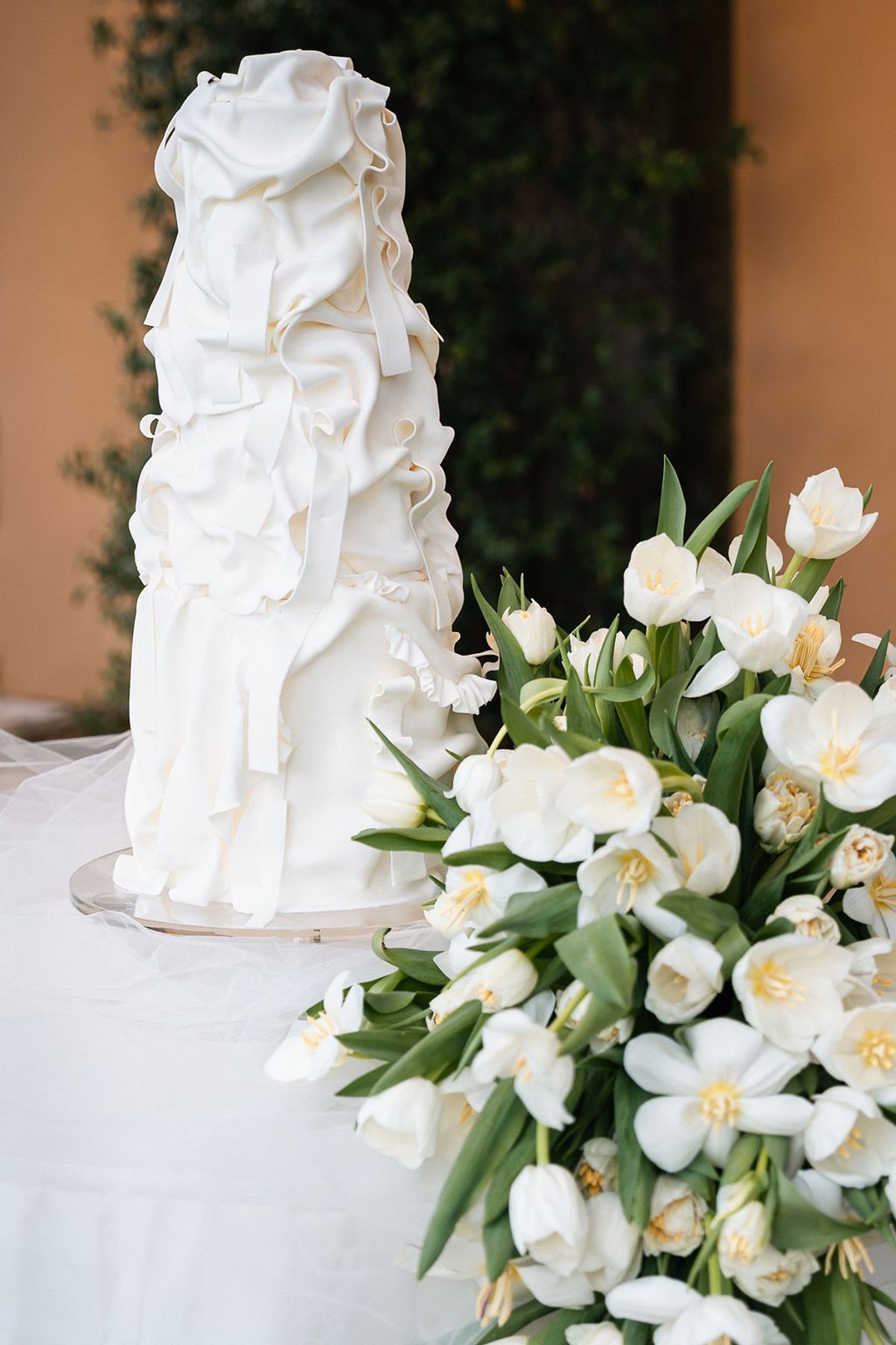Tiered white ruffled wedding cake beside an armful of white tulips and roses at Château de Sannes, Provence
