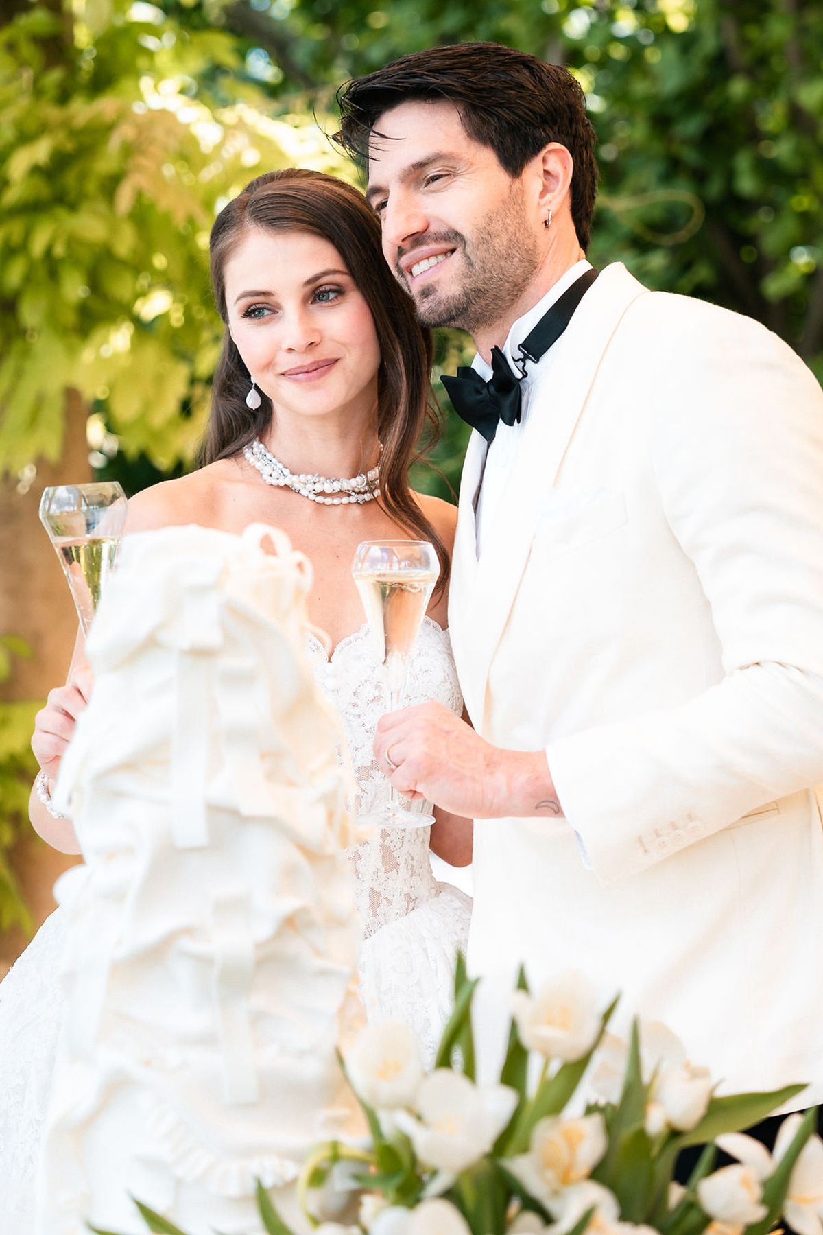 Bride and groom holding champagne flutes beside white tulips and the wedding cake at Château de Sannes, Provence