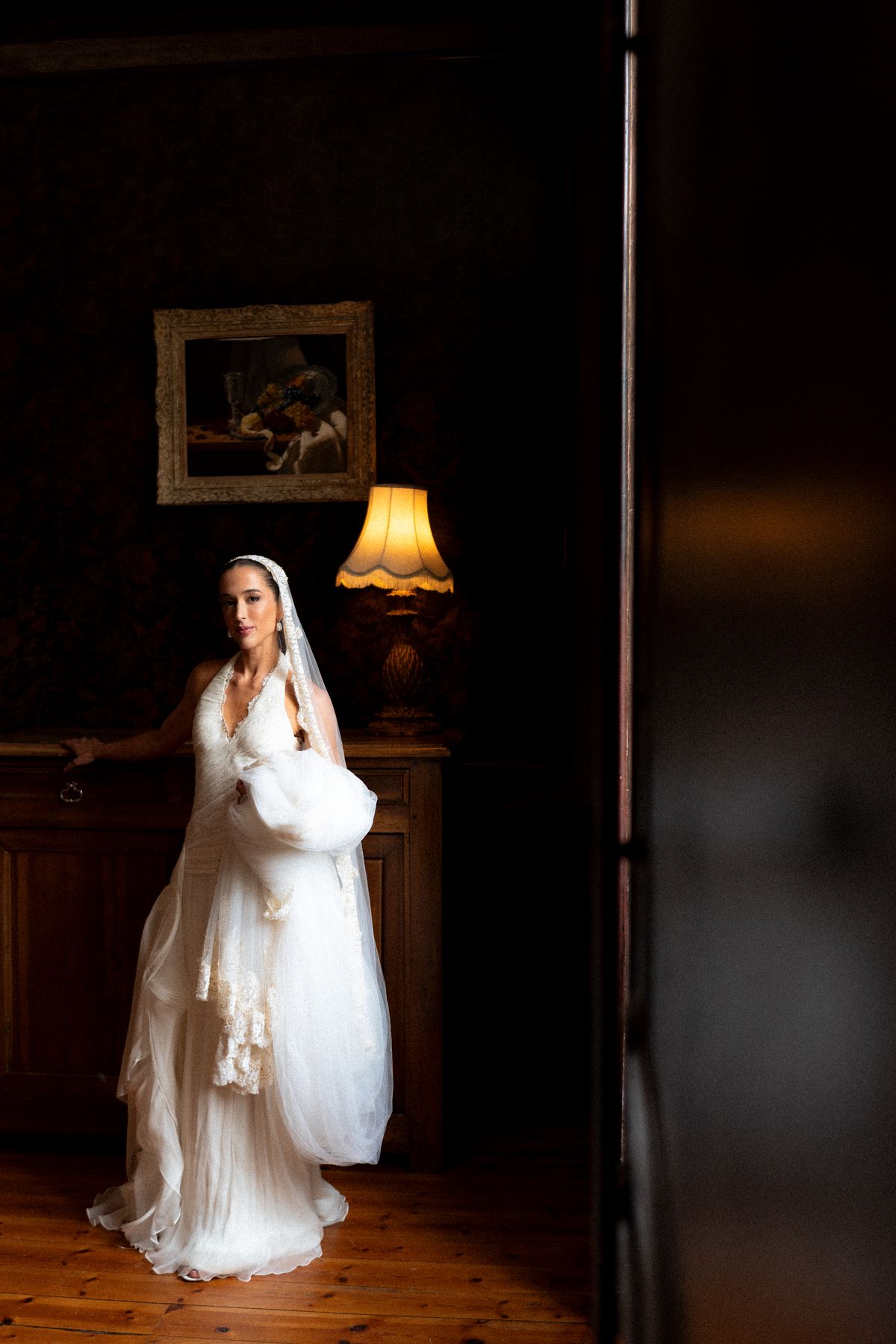 Isadora & Hugo — the bride in a doorway in warm lamplight, spring wedding in Nouvelle-Aquitaine