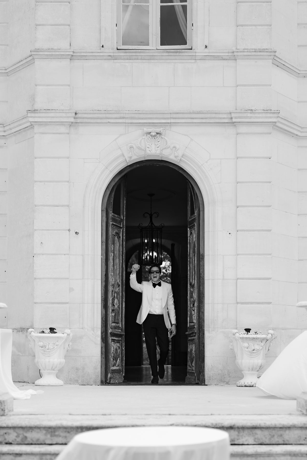 Isadora & Hugo — the couple in the chateau doorway seen from the garden, spring wedding in Nouvelle-Aquitaine