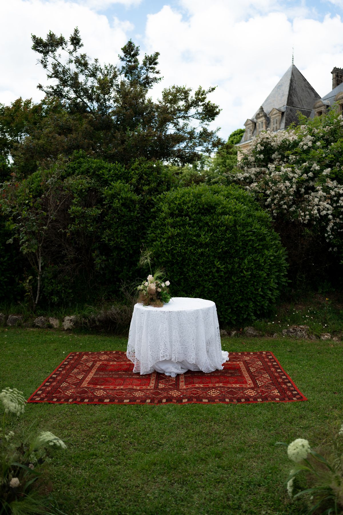 Isadora & Hugo — a small linen-covered table on a patterned rug in the garden, spring wedding in Nouvelle-Aquitaine