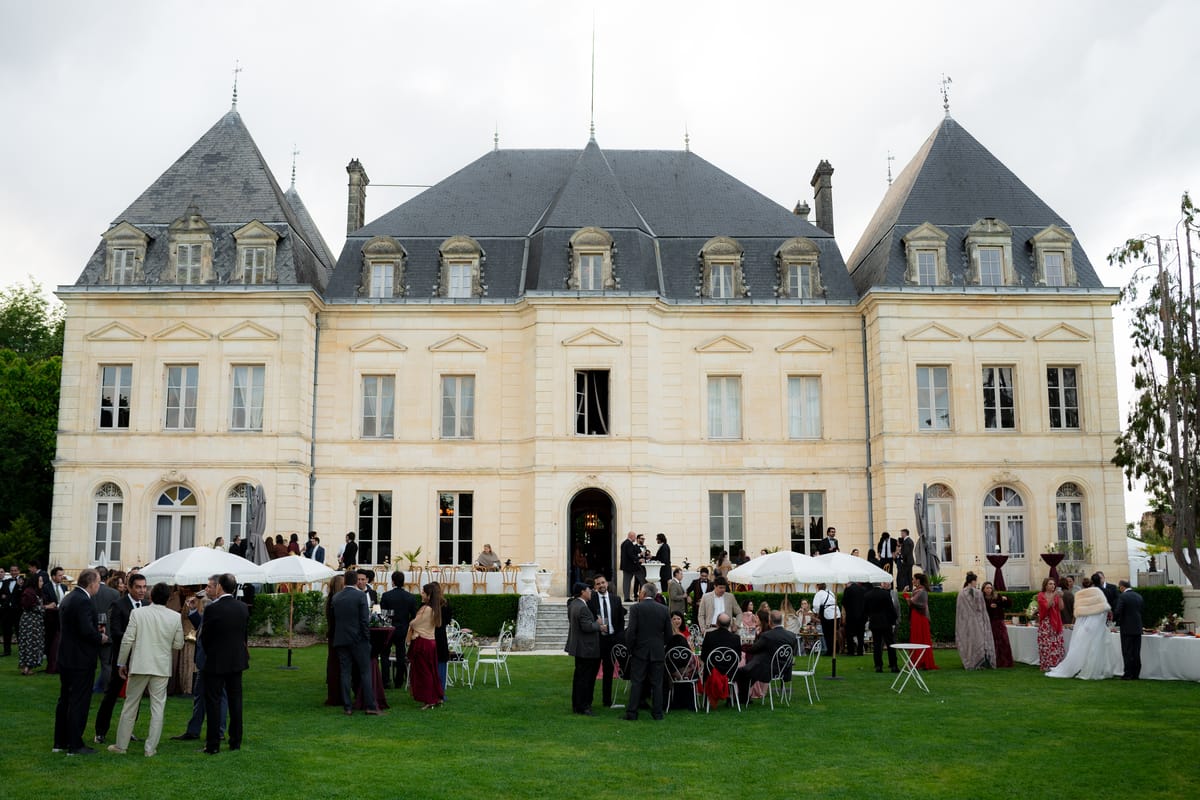 Isadora & Hugo — the chateau with guests gathered on the lawn beneath parasols, spring wedding in Nouvelle-Aquitaine