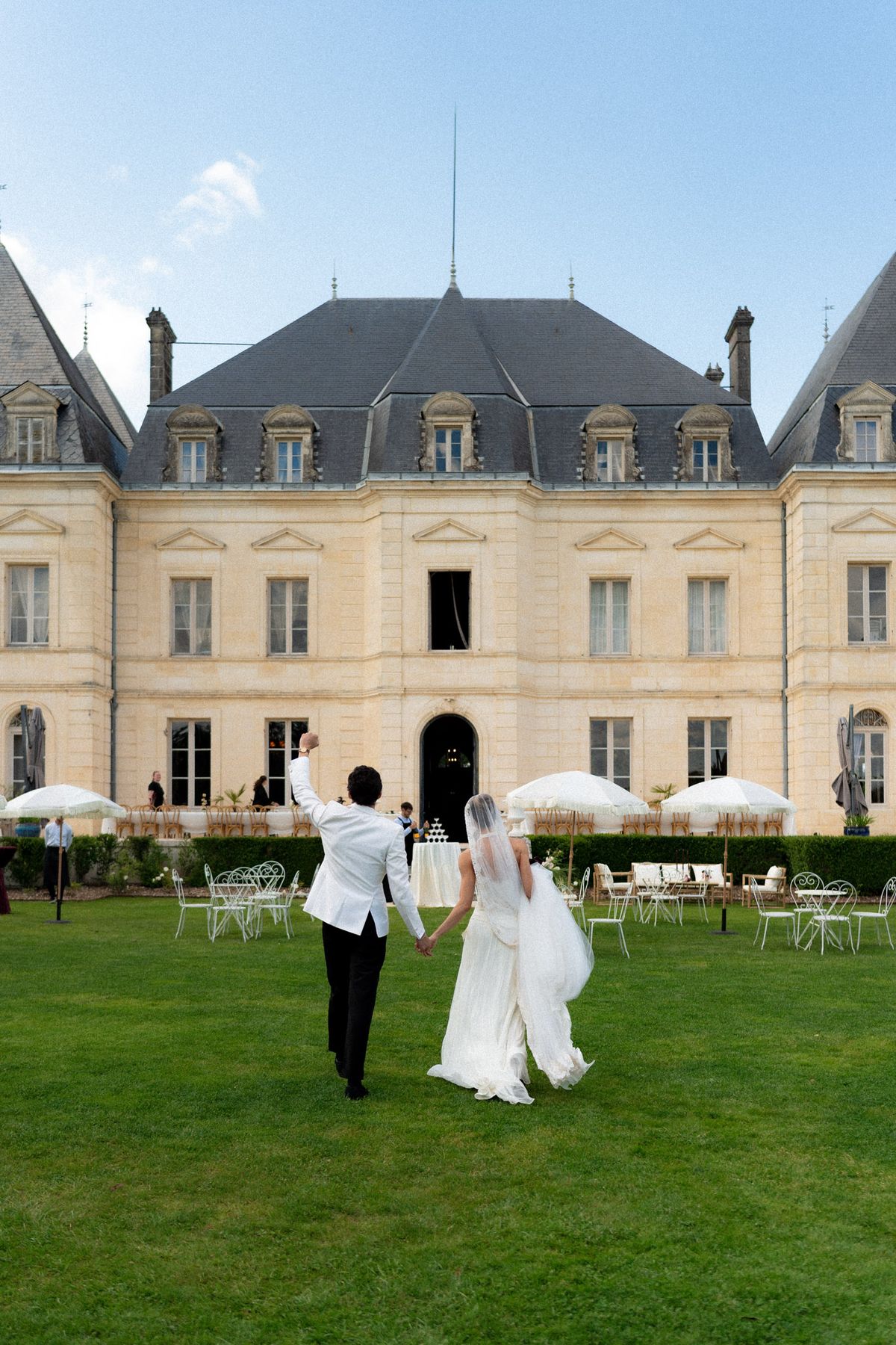 Isadora & Hugo — the couple crossing the lawn toward the chateau, spring wedding in Nouvelle-Aquitaine
