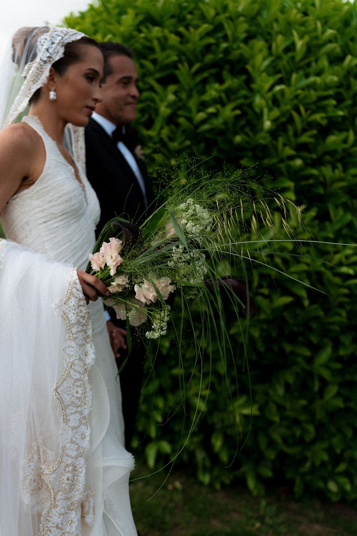 Isadora & Hugo — the couple close together beside a tall hedge, the bride holding her bouquet, spring wedding in Nouvelle-Aquitaine