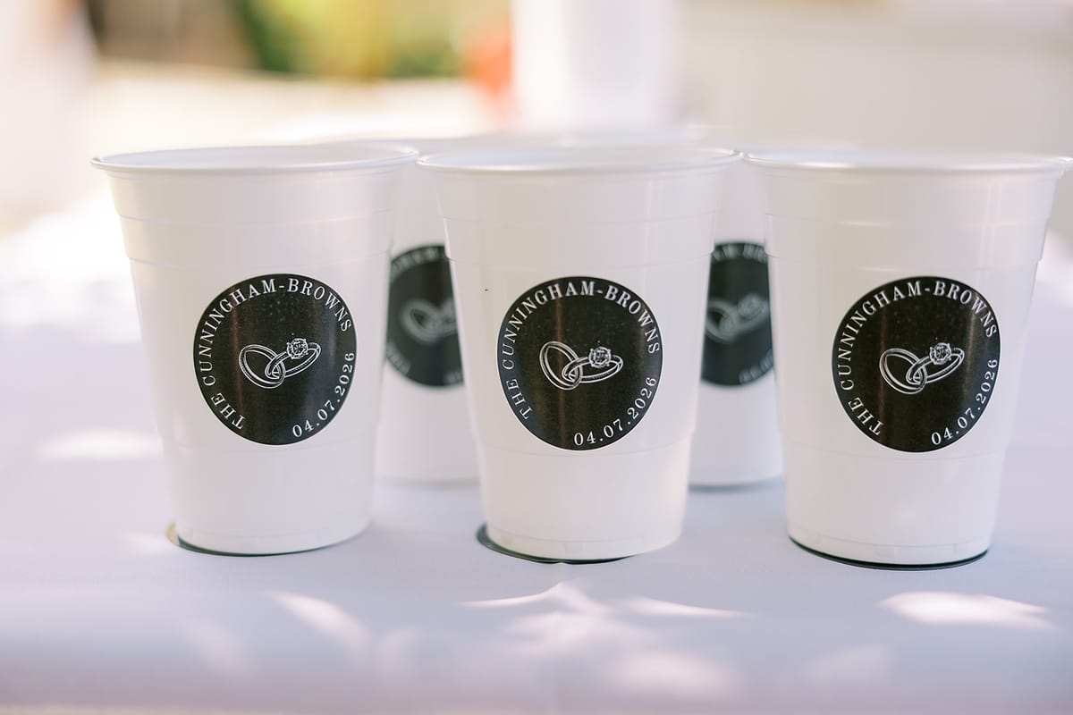 Several white paper cups with round black printed badges stand together on a white table in soft light.