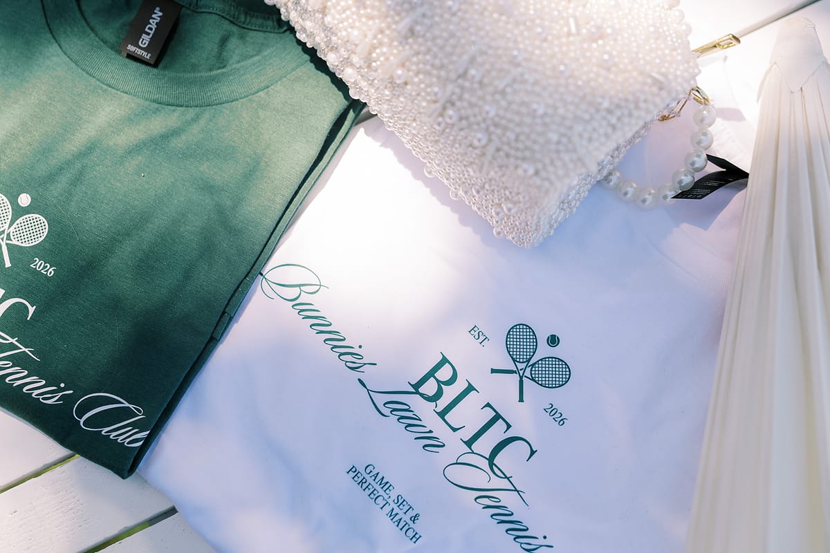 A green shirt and a white shirt with tennis club logos lie on a white surface beside a beaded fabric and a white dress.
