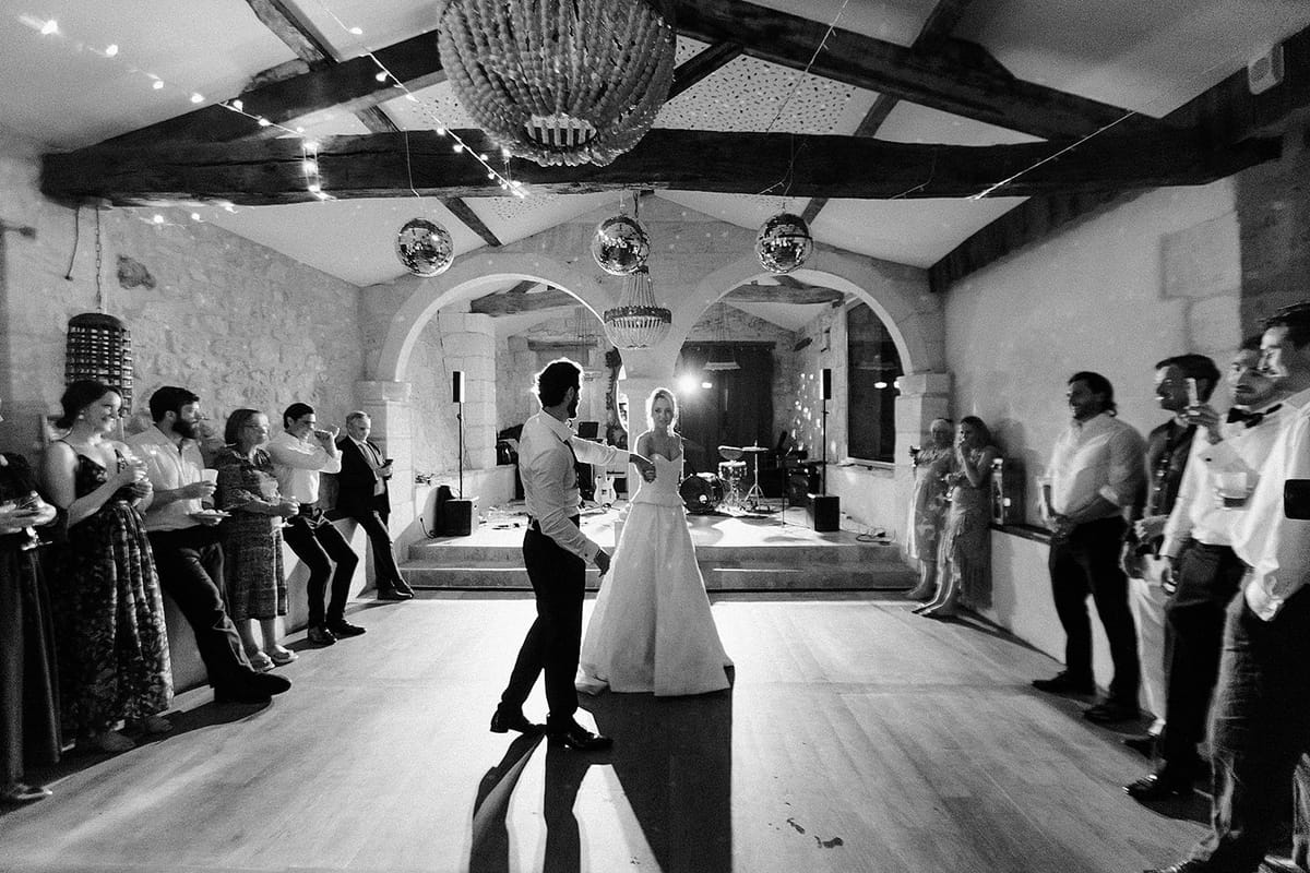 In black and white, the couple dance in the middle of a stone-walled barn while guests line the edges of the floor.