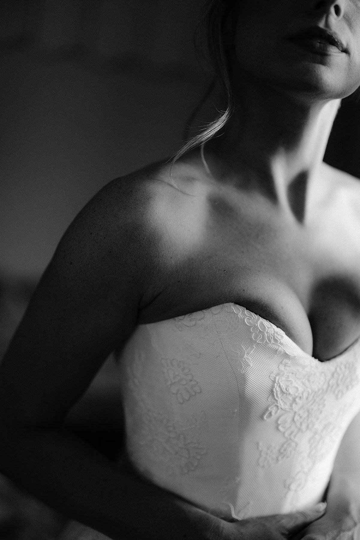 In black and white, a close crop shows the bride's shoulders and the lace-detailed bodice of a strapless gown.