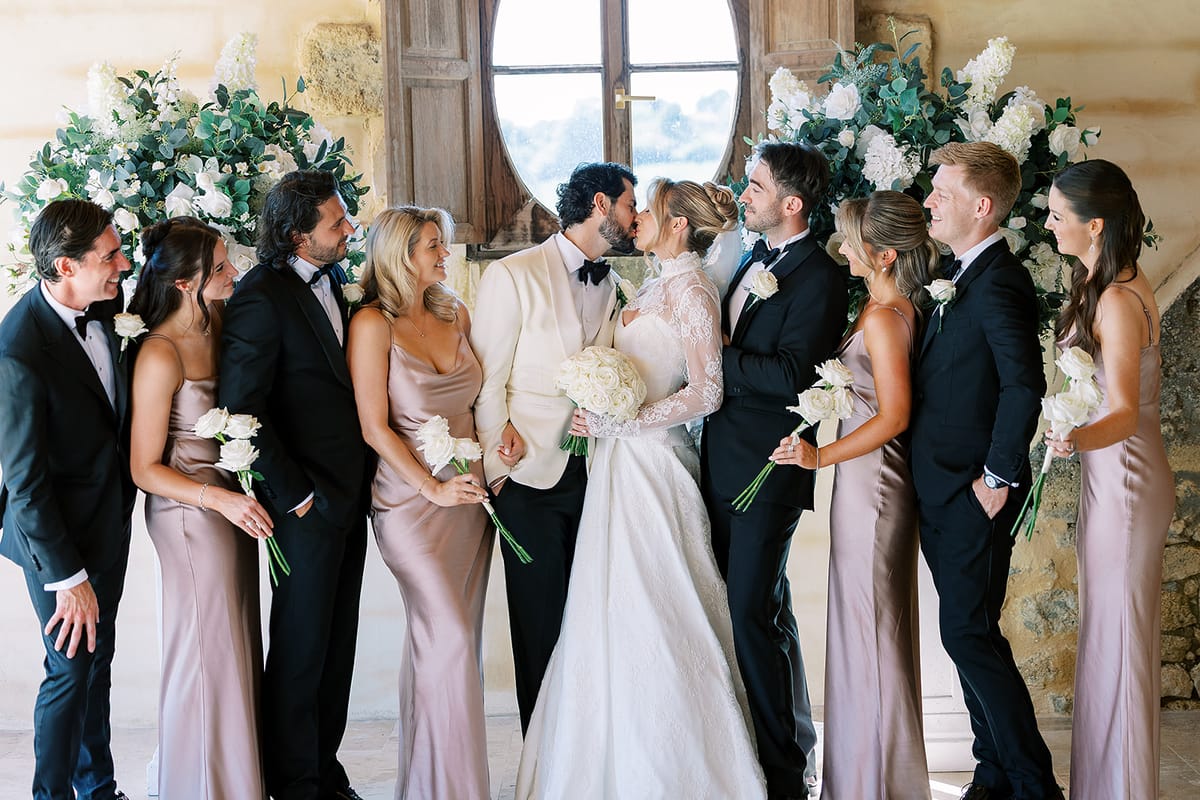 The couple kiss in the centre of a group of bridesmaids in mauve satin dresses and groomsmen in black tuxedos.