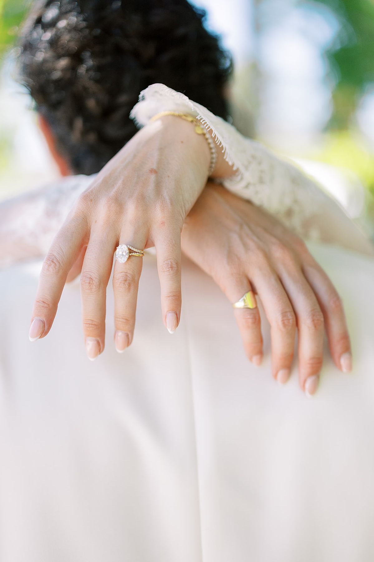 Close-up of the bride's manicured hand wearing a ring and bracelet, resting on the groom's shoulder as they embrace.