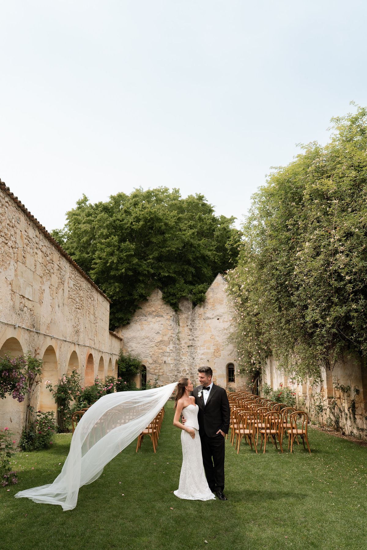 Jori and JD walking hand in hand through a stone archway, her veil trailing behind