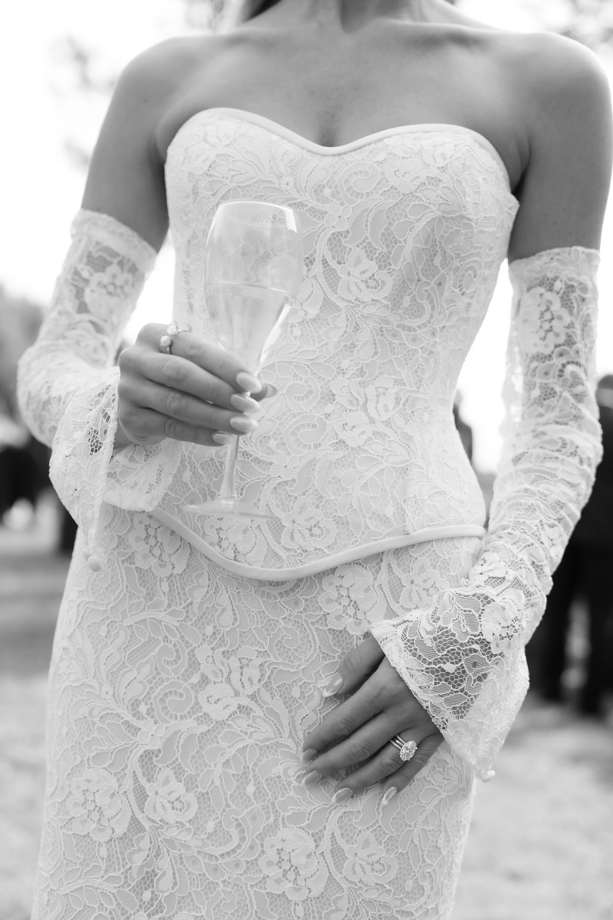 A detail of Jori's lace gown and long gloves as she holds a champagne glass
